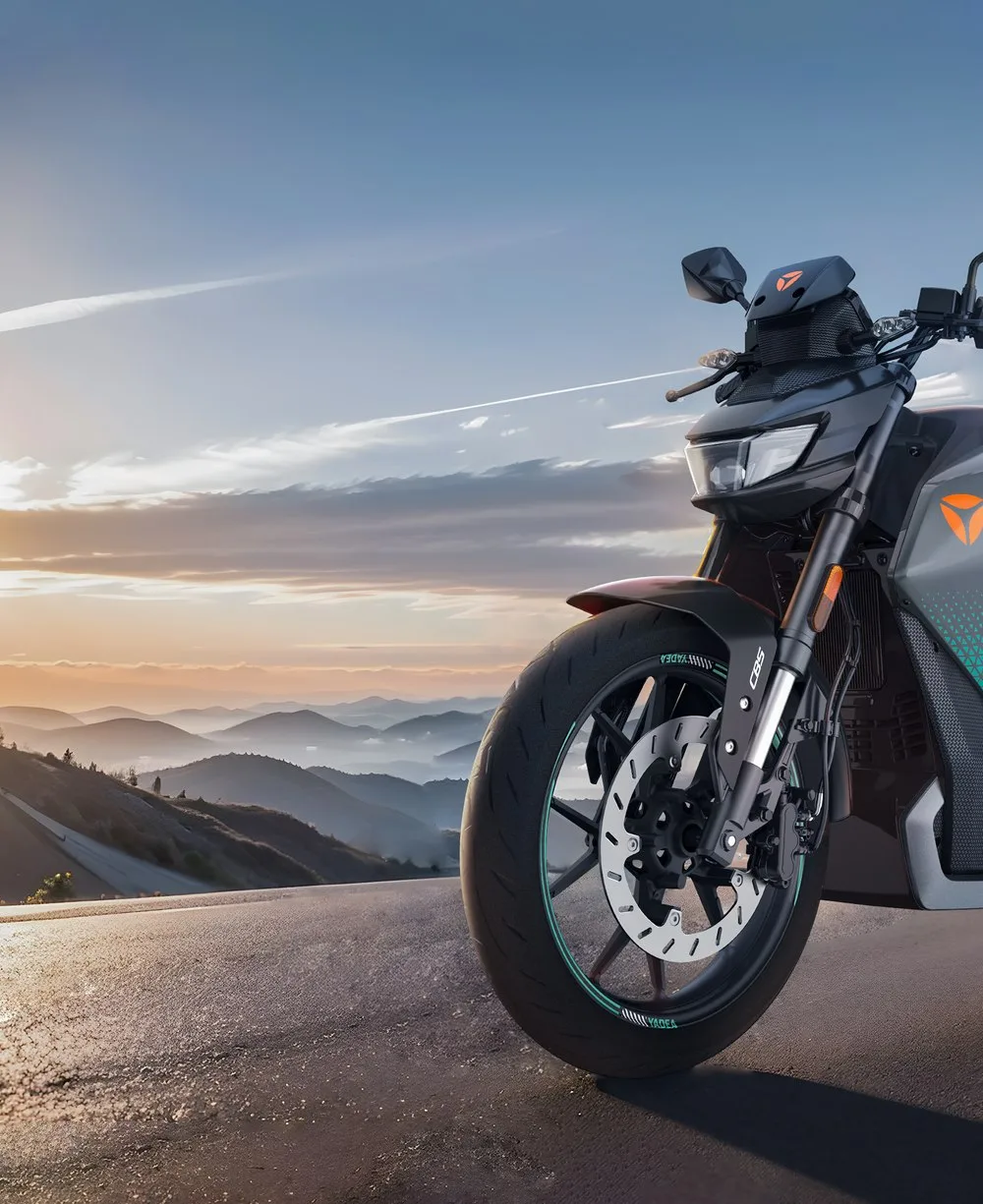 Motocicleta elétrica Yadea escura numa estrada de serra ao entardecer